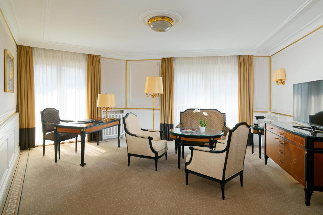 מלון The Westin Grand ברלין מראה חיצוני תמונה The photo depicts a well-designed room, likely a hotel suite or an upscale living space. It features two large windows covered with light-colored drapes, allowing natural light to fill the room. The flooring appears to be carpeted, contributing to a 