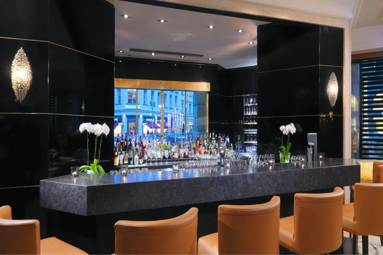 מלון The Westin Grand ברלין מראה חיצוני תמונה The photo depicts a modern bar area with a sleek and elegant design. The bar counter is made of dark stone, and behind it is a well-stocked bar shelf featuring various bottles of alcohol. The backdrop is decorated with black panels, giving it a luxur