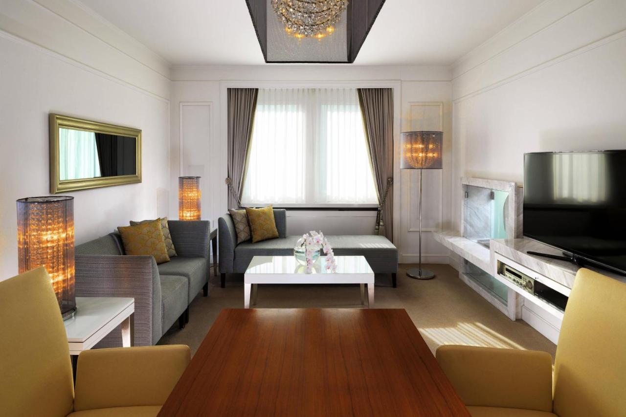 מלון The Westin Grand ברלין מראה חיצוני תמונה The photo depicts a modern and elegantly designed living room. The space features:

- A comfortable seating area with a light gray sectional sofa and decorative cushions.
- A central white coffee table.
- Two stylish floor lamps adding warm lighting 