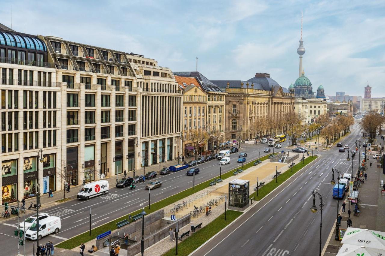 מלון The Westin Grand ברלין מראה חיצוני תמונה The photo shows a wide urban street with a mix of modern and historic buildings on either side. The foreground features a wide road with traffic, including cars and vans. On the left, there are contemporary architectural designs, while on the right, 