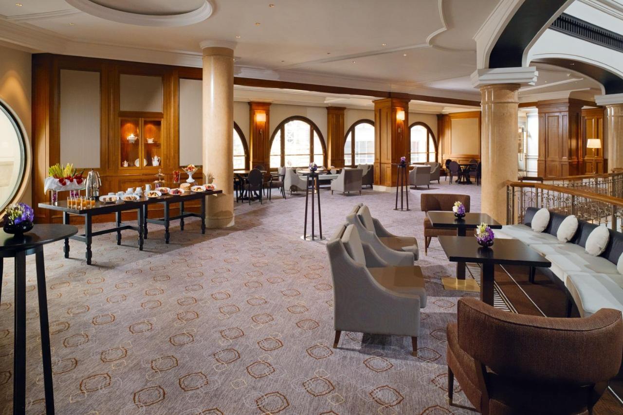 מלון The Westin Grand ברלין מראה חיצוני תמונה The photo shows a spacious and elegantly designed interior of a lounge or reception area. The room features large arched windows that allow natural light to fill the space. There are a mix of comfortable seating arrangements, including plush armchair