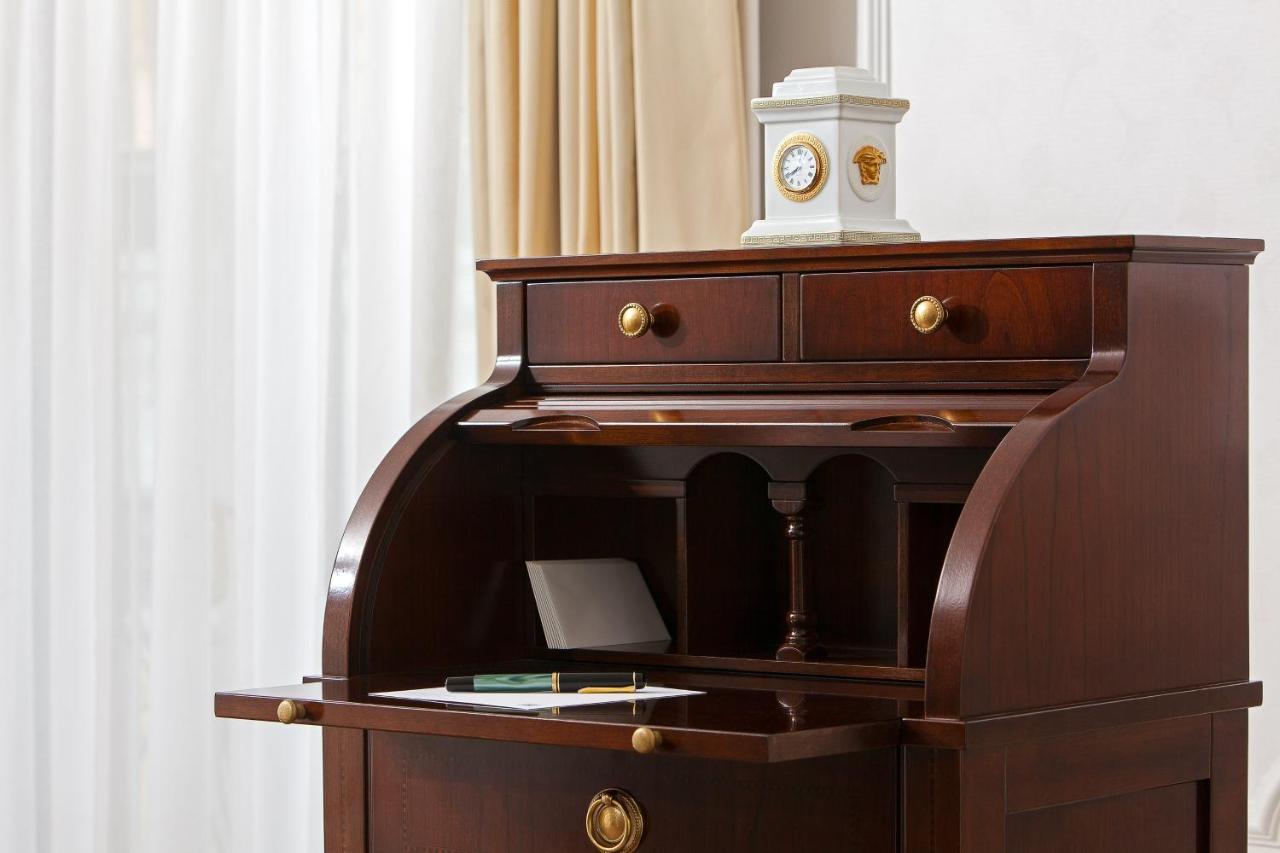מלון The Westin Grand ברלין מראה חיצוני תמונה The image shows a wooden writing desk with a rich, dark finish. The desk features a curved front and an open compartment above a flat writing surface. There are two small drawers at the top, each with round brass handles. On the desk, there is a shee