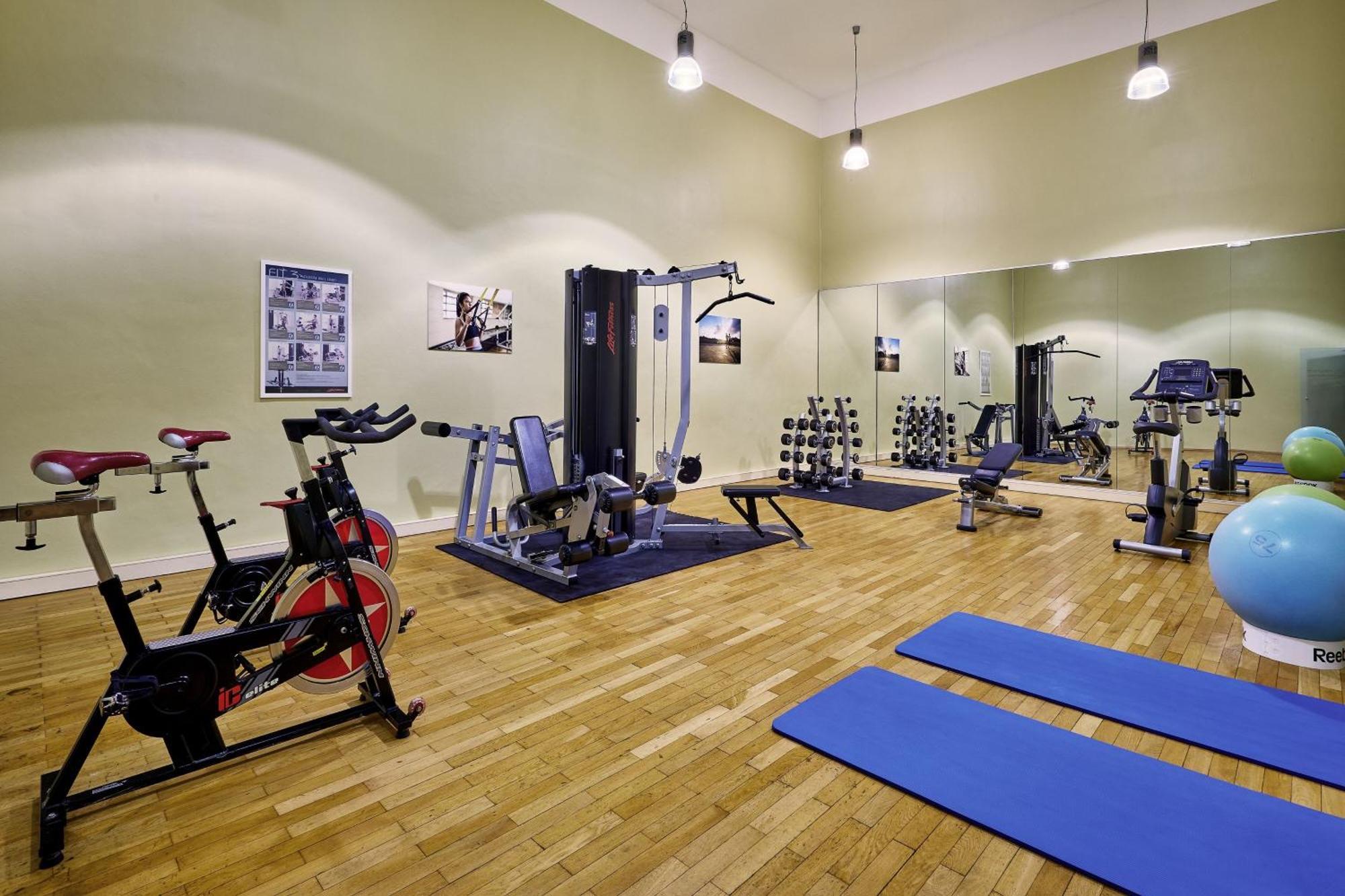 מלון The Westin Grand ברלין מראה חיצוני תמונה The photo depicts a fitness or workout room. It features various exercise equipment, including:

- A stationary bike on the left.
- A multi-gym machine in the center, designed for different strength training exercises.
- A set of free weights organiz