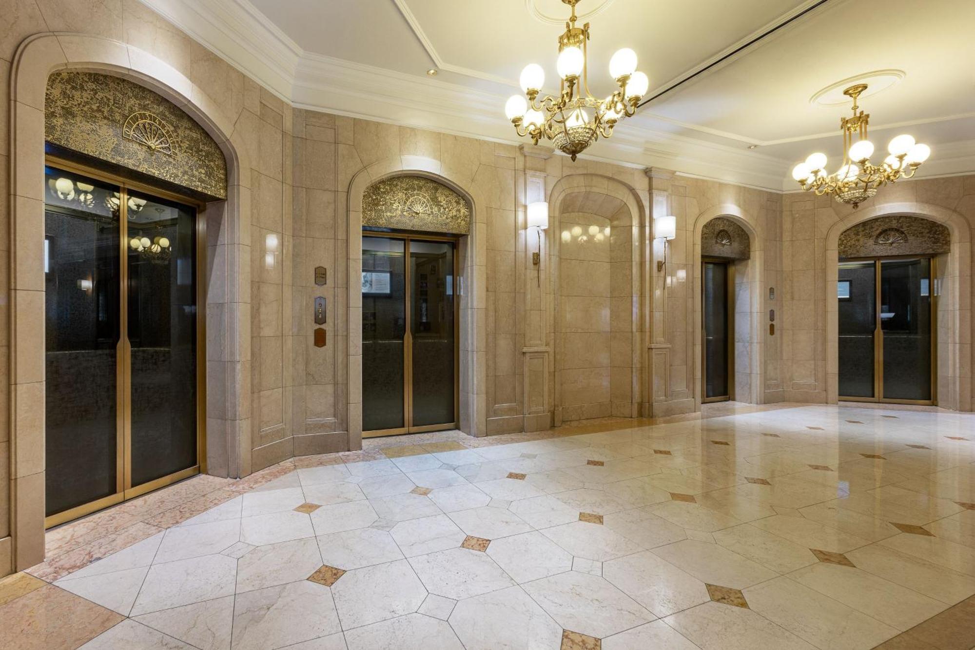 מלון The Westin Grand ברלין מראה חיצוני תמונה The photo shows an elegant lobby area with several glass elevators. The walls are finished with light-colored stone, giving a polished and upscale look. The ceiling features ornate chandeliers that add to the luxurious atmosphere. The floor is tiled 